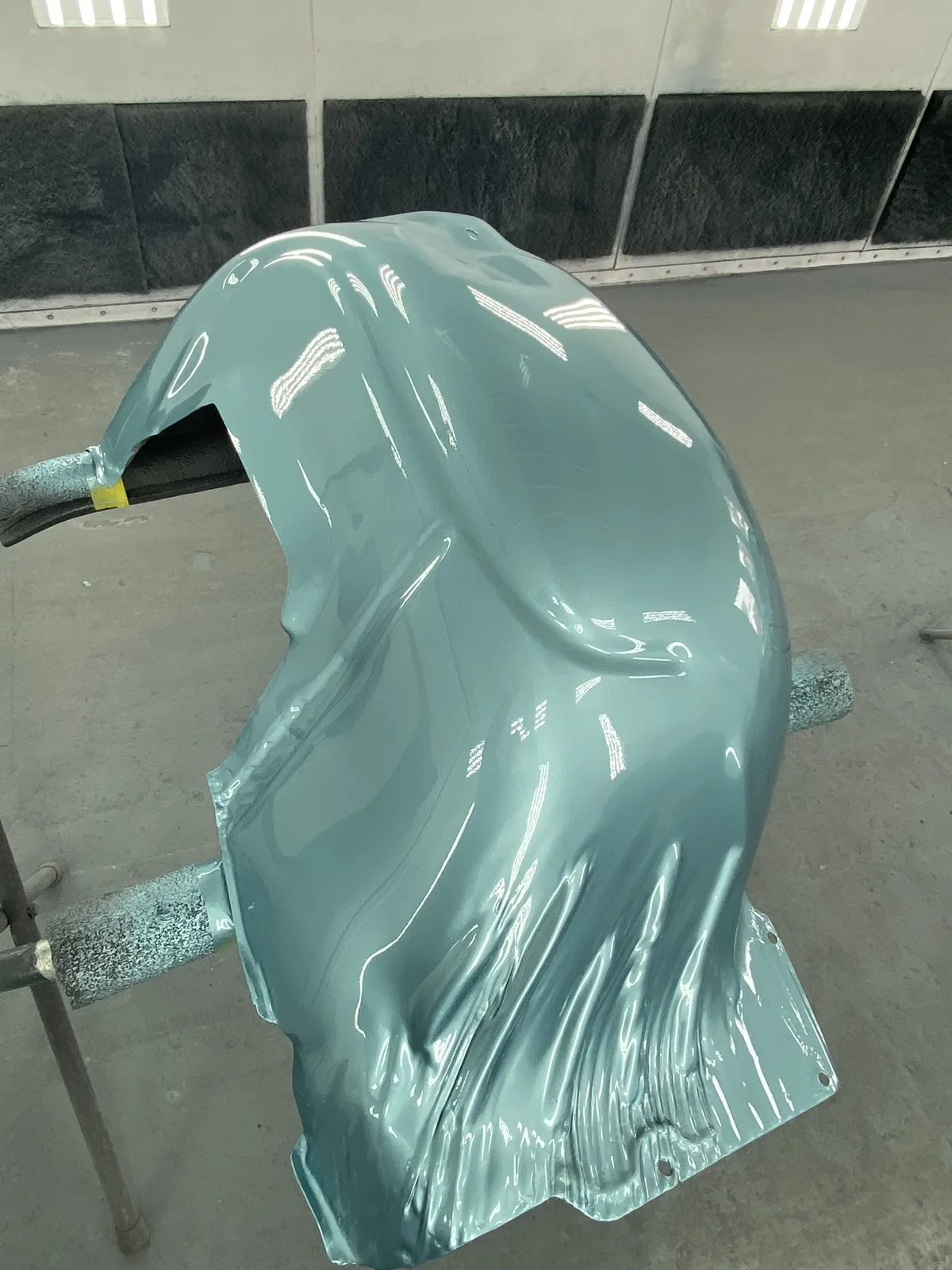 Teal car hood with smooth gloss finish on paint stand